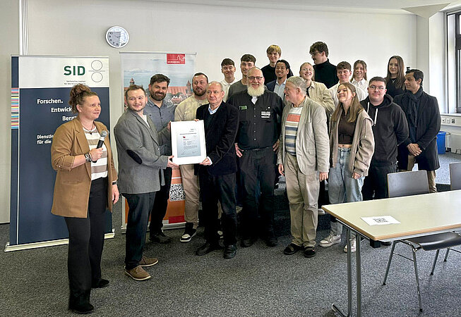 Carolin Sommerer und Alexander Bartel (SID) übergeben die neue PSO-Urkunde an Kai-Uwe Arnold (hauptverantwortlicher Lehrer an der B6, fünfter von links) PSO-B6-2026